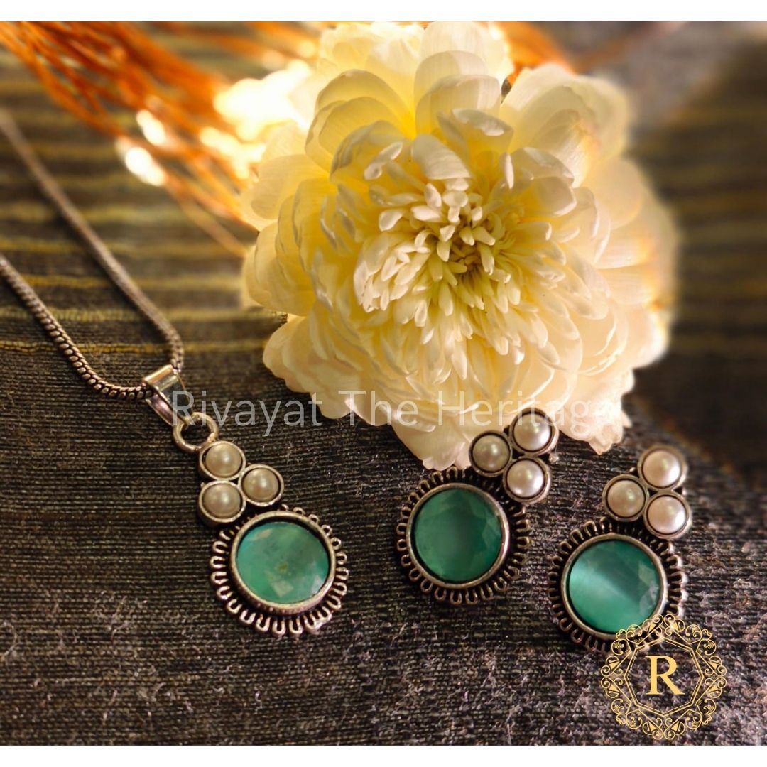 Emerald green Monalisa stone oxidized German silver earrings and pendant jewelry set by Rivayat The Heritage Manika collection on wooden background with white flower