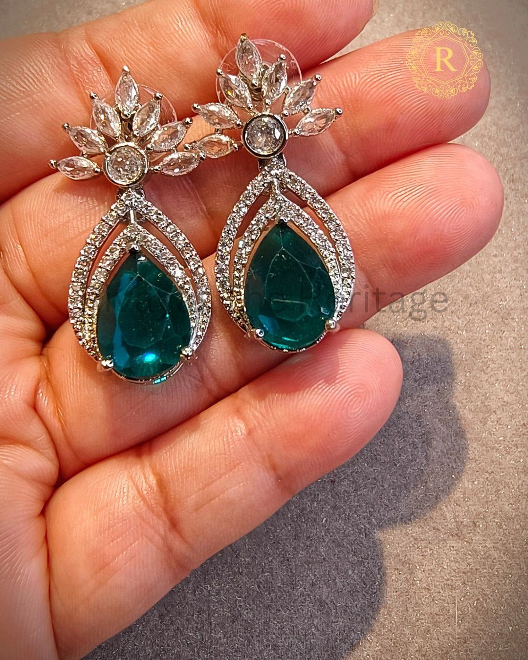Emerald zircon diamond drop earrings with silver rhodium finish held in hand