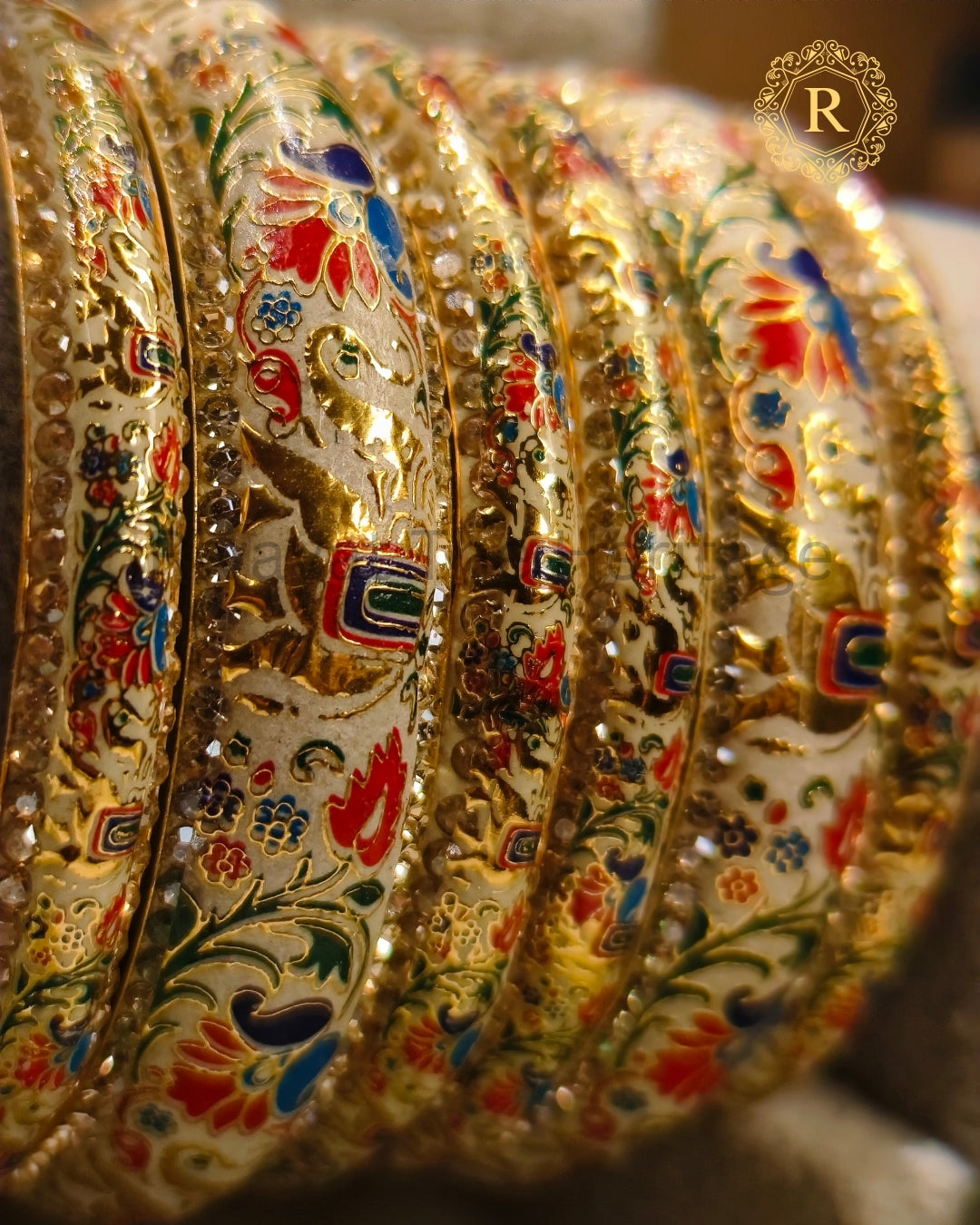 Close-up of handcrafted ivory Meenakari bangles with red, blue and green peacock floral enamel work and stone border