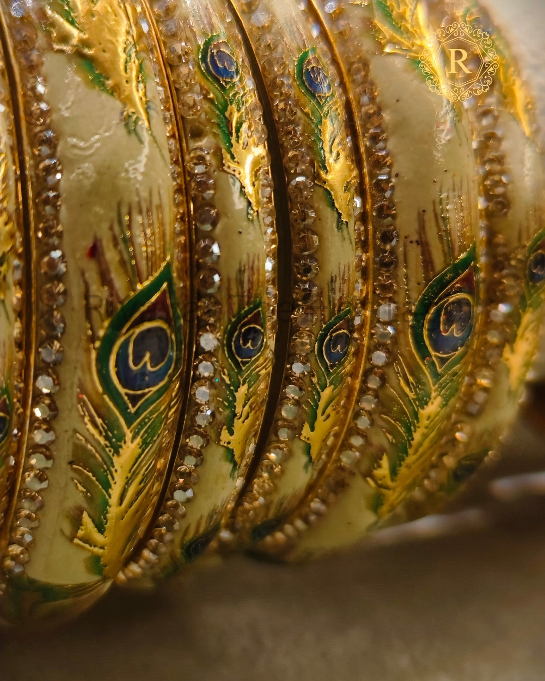 Close-up of ivory Meenakari bangles with hand-painted peacock feather design and stone-studded border