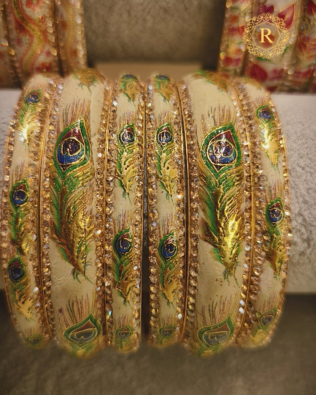 Stack of ivory Meenakari bangles showing gold peacock feather motifs and kundan stone detailing