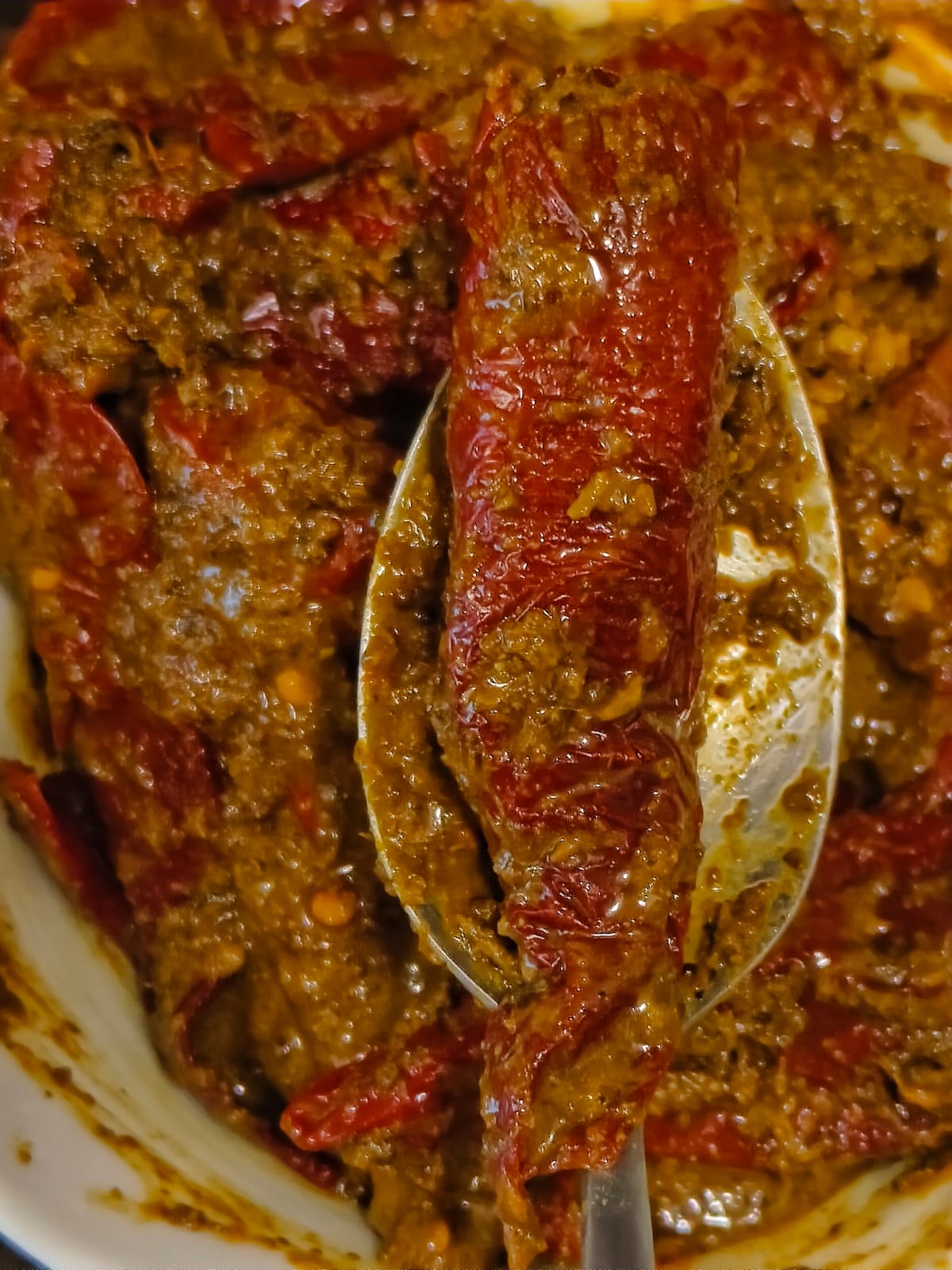 Spoon lifting a whole stuffed red chilli from Rivayat's homemade Banarasi Lal Mirch Bharua pickle