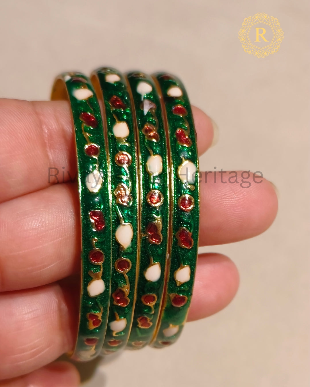 Close-up of handcrafted green Meenakari bangles showing red and white enamel detailing on gold-tone base