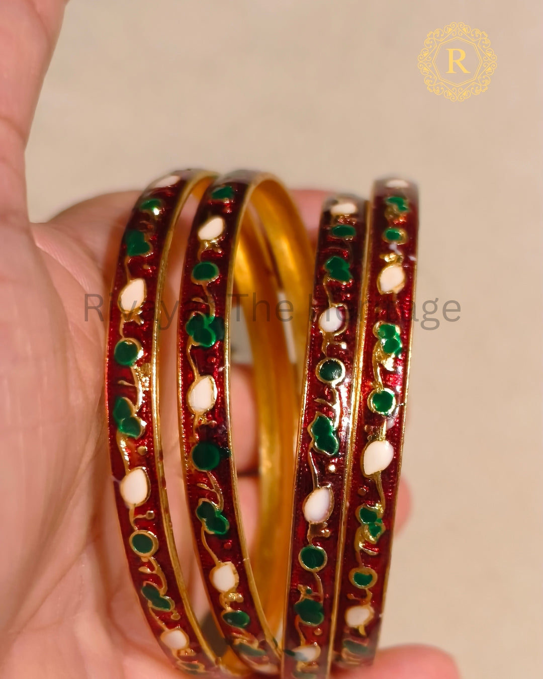 Red Meenakari bangles set of 2 held in hand, showing green and white enamel detailing on gold-toned metal