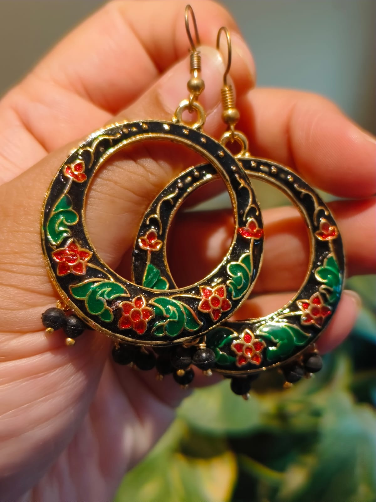 Close-up of black Meenakari hoop earrings showing red enamel flowers, green leaf motifs, gold outline and black bead fringe – Rivayat Heritage