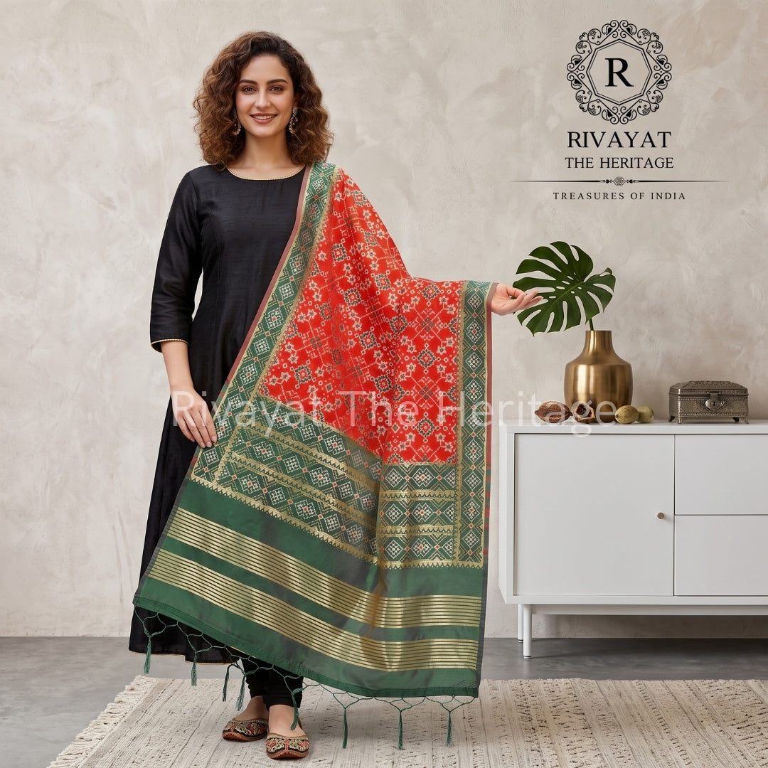 A smiling model wearing a black kurti, elegantly draped in a vibrant red and green traditional Indian dupatta with intricate geometric patterns and a gold border by Rivayat The Heritage.